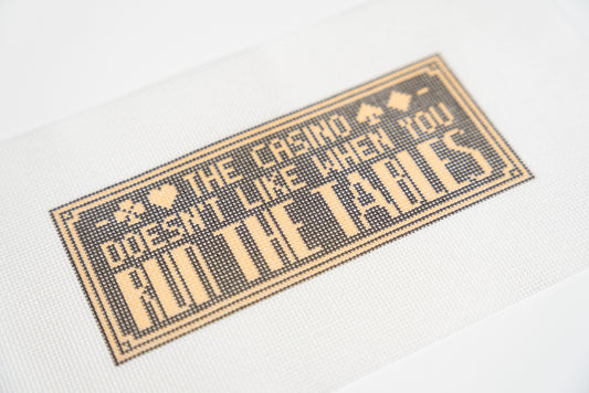 Close angled view of the run the tables lettering, card suits and double gold border on 13 mesh canvas