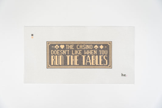 Run the Tables needlepoint canvas, soft gold lettering on a charcoal panel with a deco border and card suits, 13 mesh, full view