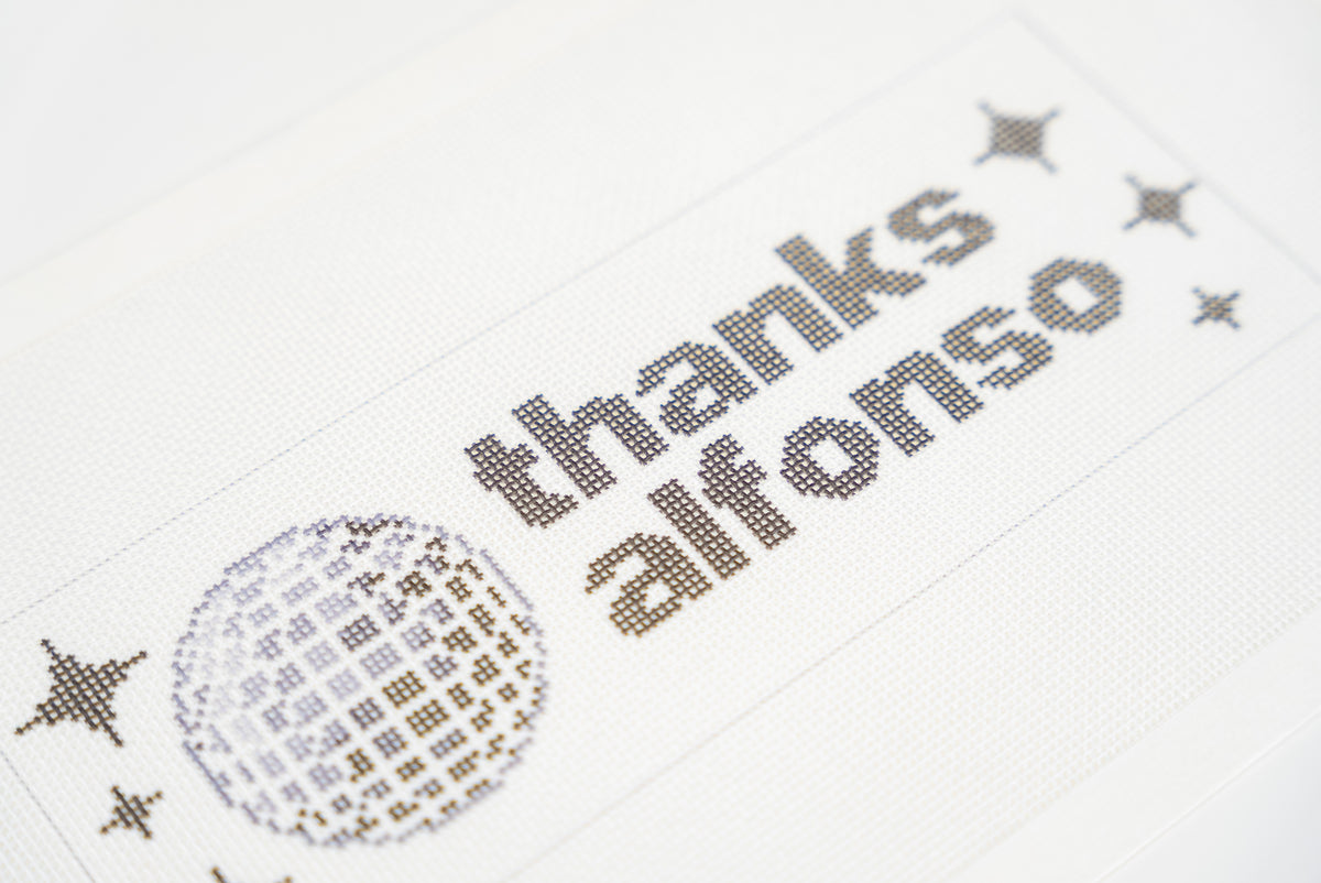 Printed needlepoint canvas reading thanks alfonso, close angled view of the letters and disco ball on 18 mesh
